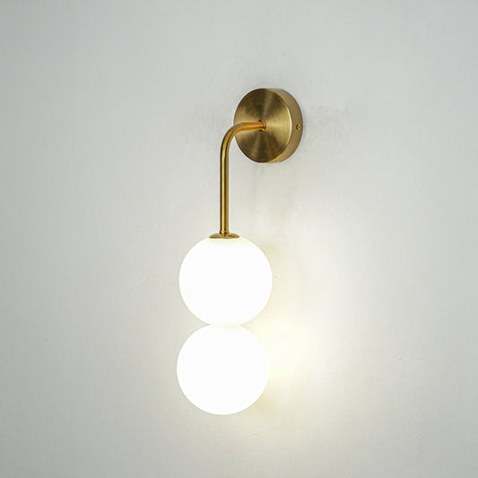 Modern wall light with gold finish and single white glass globe on neutral background minimal lighting perfect for bedroom decor.

