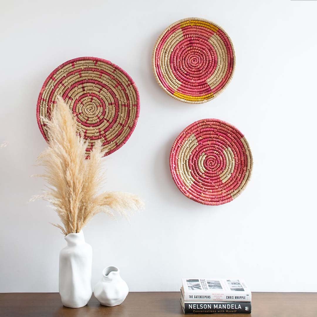 Boho-style handwoven wall basket displayed on a living room wall above a wooden console with vases and books.