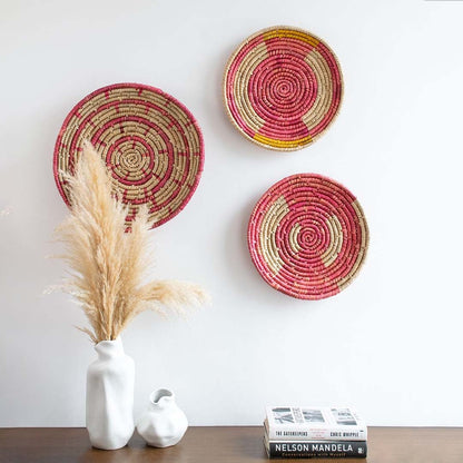 Boho-style handwoven wall basket displayed on a living room wall above a wooden console with vases and books.