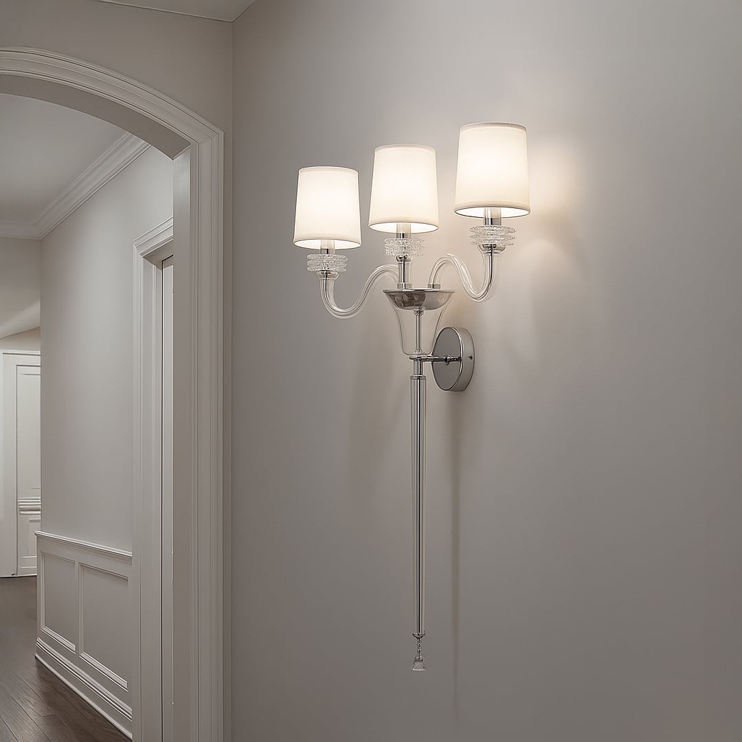 Triple arm wall light with chrome base and fabric shades glowing in modern hallway with neutral wall decor.