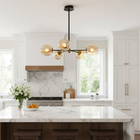 Modern chandelier with glass globe lights in gold finish hanging above kitchen island adding warm ambient lighting to elegant home interior.