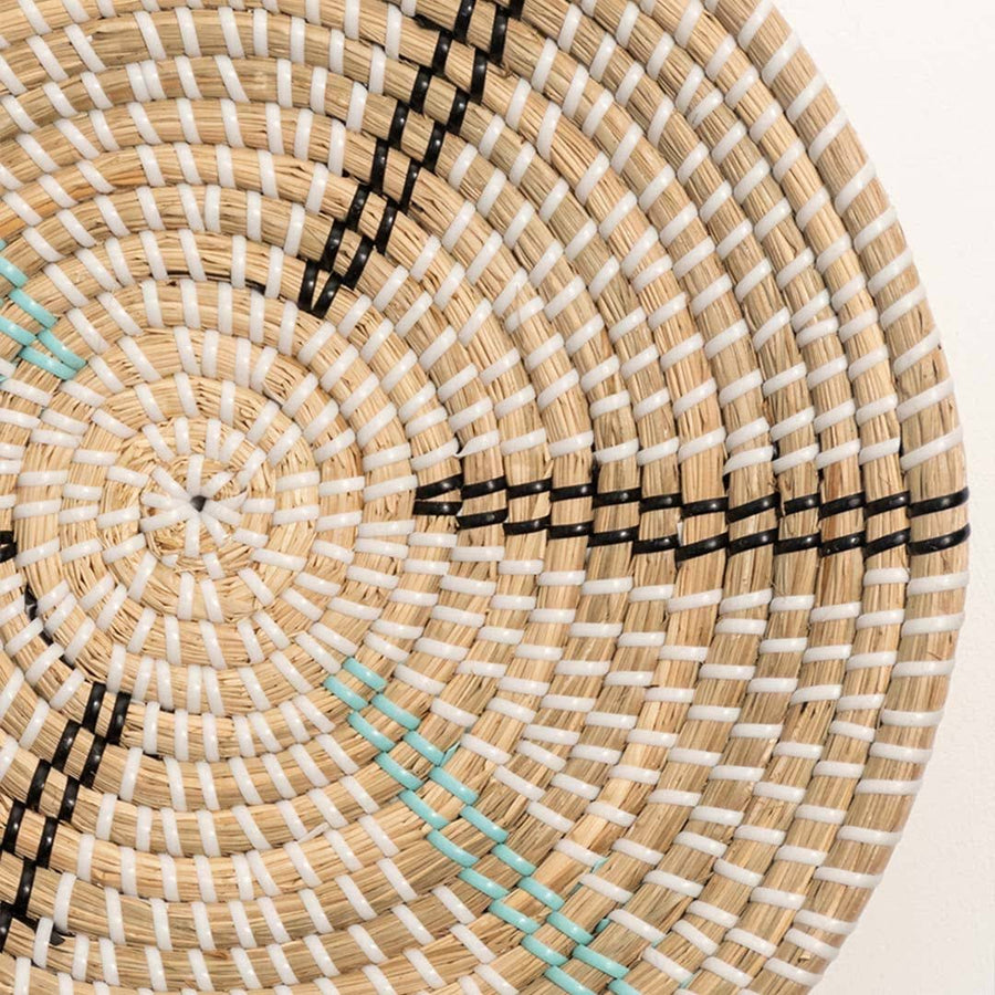Detailed closeup of handcrafted natural cream seagrass wall basket with black and teal woven spokes for boho decor.