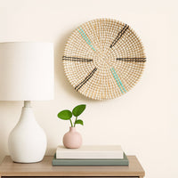 Handcrafted circular wall decor in neutral tones placed above console table with vases creating calm minimalist living room styling.