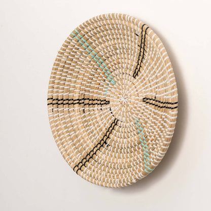Side view of handcrafted natural cream seagrass wall basket with black and teal striped spokes for boho wall decor.