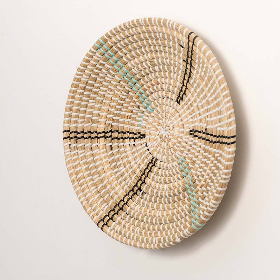 Side view of handcrafted natural cream seagrass wall basket with black and teal striped spokes for boho wall decor.