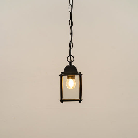Black metal hanging outdoor lantern with square glass enclosure glowing on white background suitable for porch entrance and exterior decor lighting.