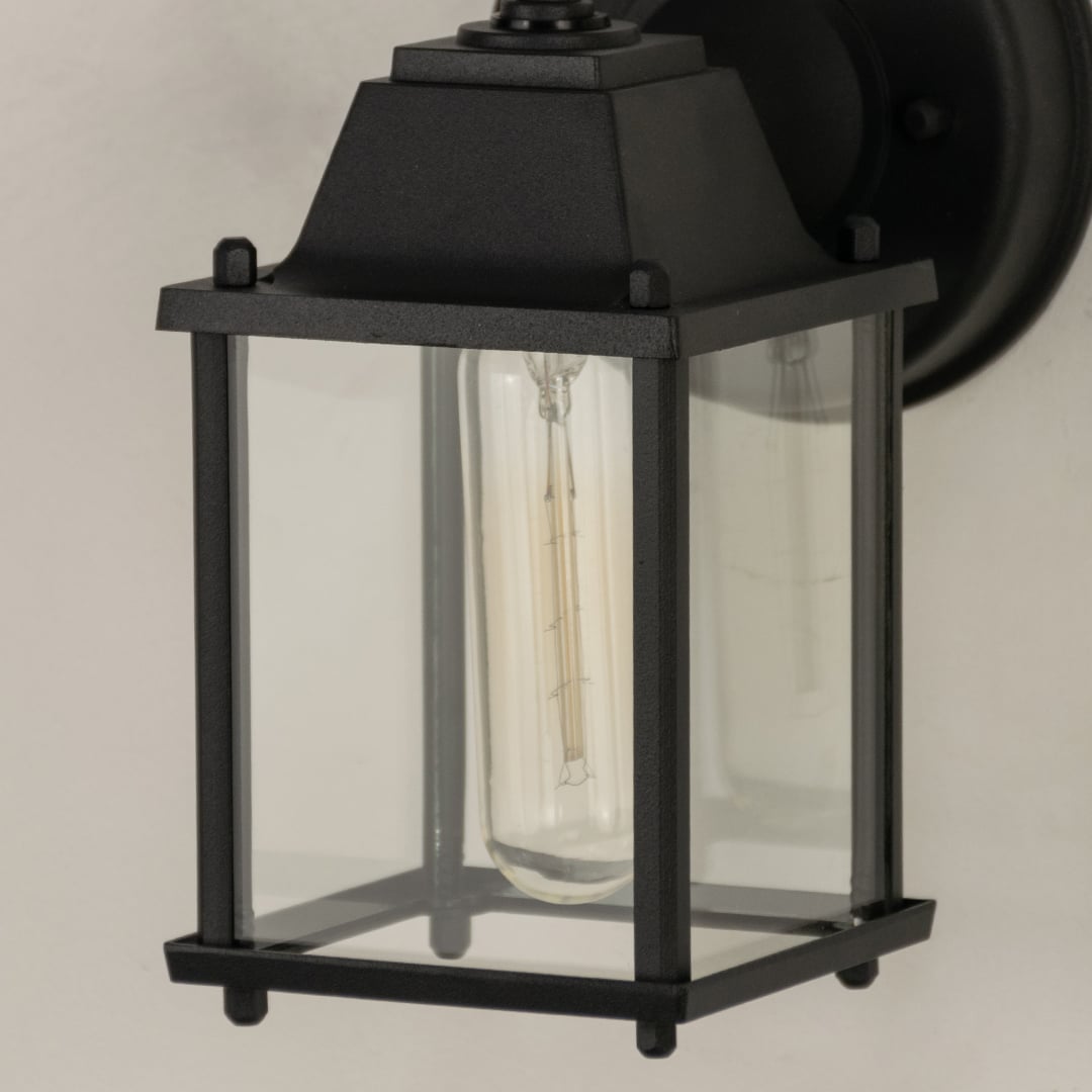 A closeup view of the outdoor wall light showing the glass panels and metal detailing with clear visibility of the bulb and smooth frame finish.
