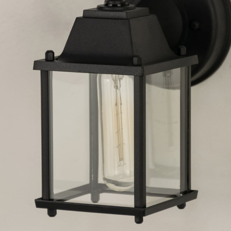 A closeup view of the outdoor wall light showing the glass panels and metal detailing with clear visibility of the bulb and smooth frame finish.