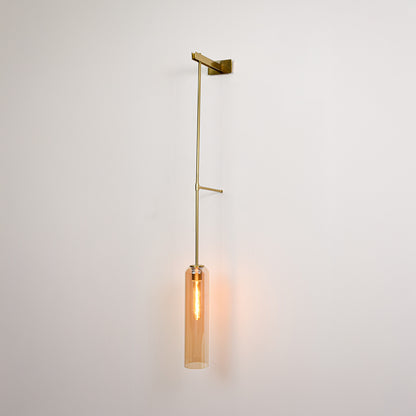 Gold metal wall light with hanging tube shade emitting warm ambient glow ideal for bedroom or hallway wall decor.