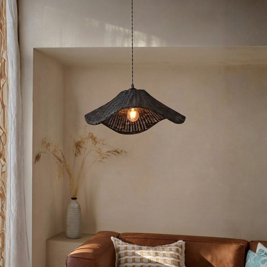 A dark woven wicker pendant light with a warm glowing bulb, hanging in a rustic, warm-toned room above a brown leather sofa.