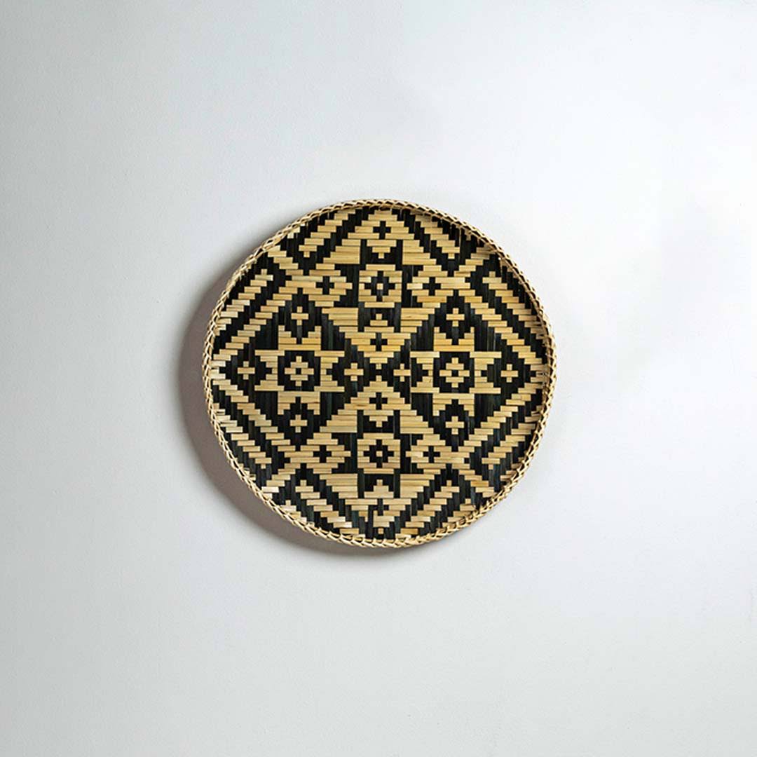 Round handcrafted black and natural seagrass wall basket with diamond pattern on white background image.
