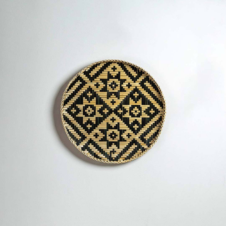 Round handcrafted black and natural seagrass wall basket with diamond pattern on white background image.