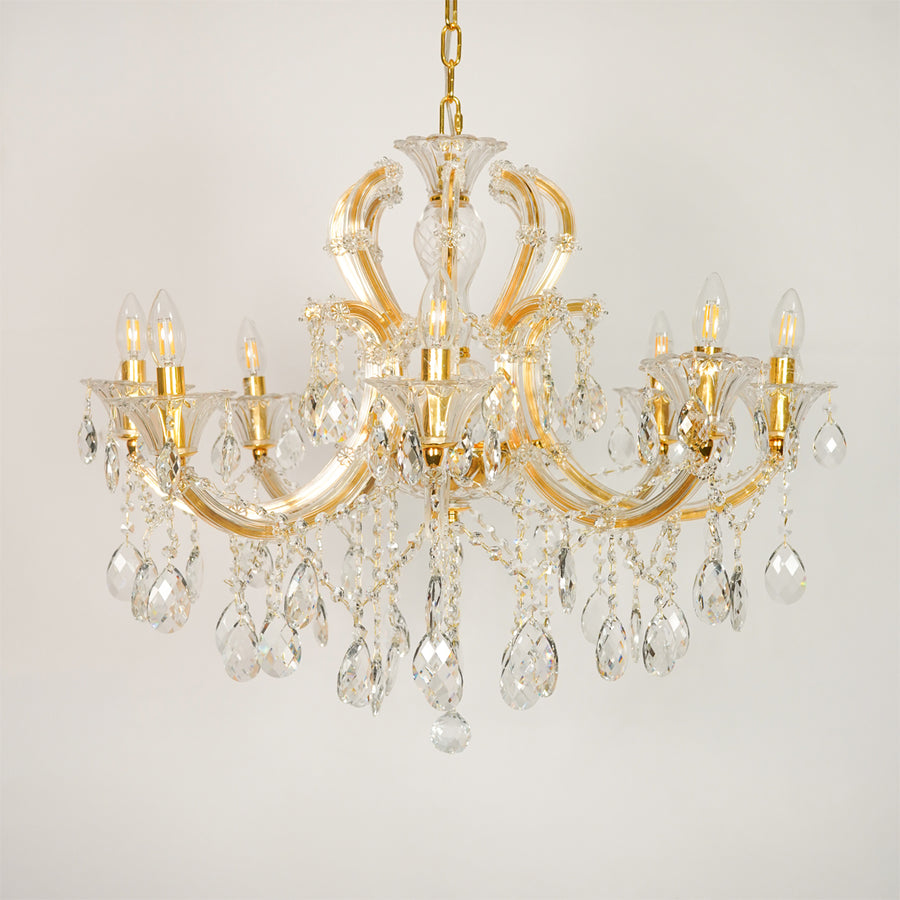 White background image of large gold metal candle style chandelier for elegant dining room decor with unlit crystal arms.