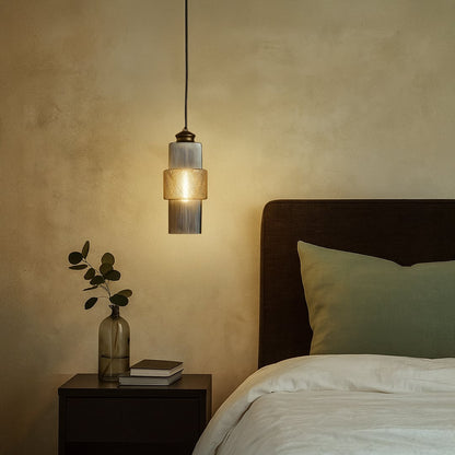 Modern pendant light with ribbed glass and brass finish glowing warmly beside bed for elegant bedroom lighting.