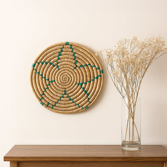 Medium beige and teal woven wall basket hanging on a white wall above a wooden console with dried flowers for modern boho decor.