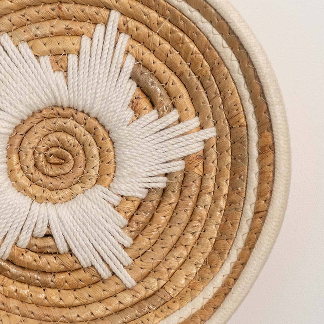 Closeup of natural seagrass wall basket with white spiral sunburst woven design for elegant artisan home décor.