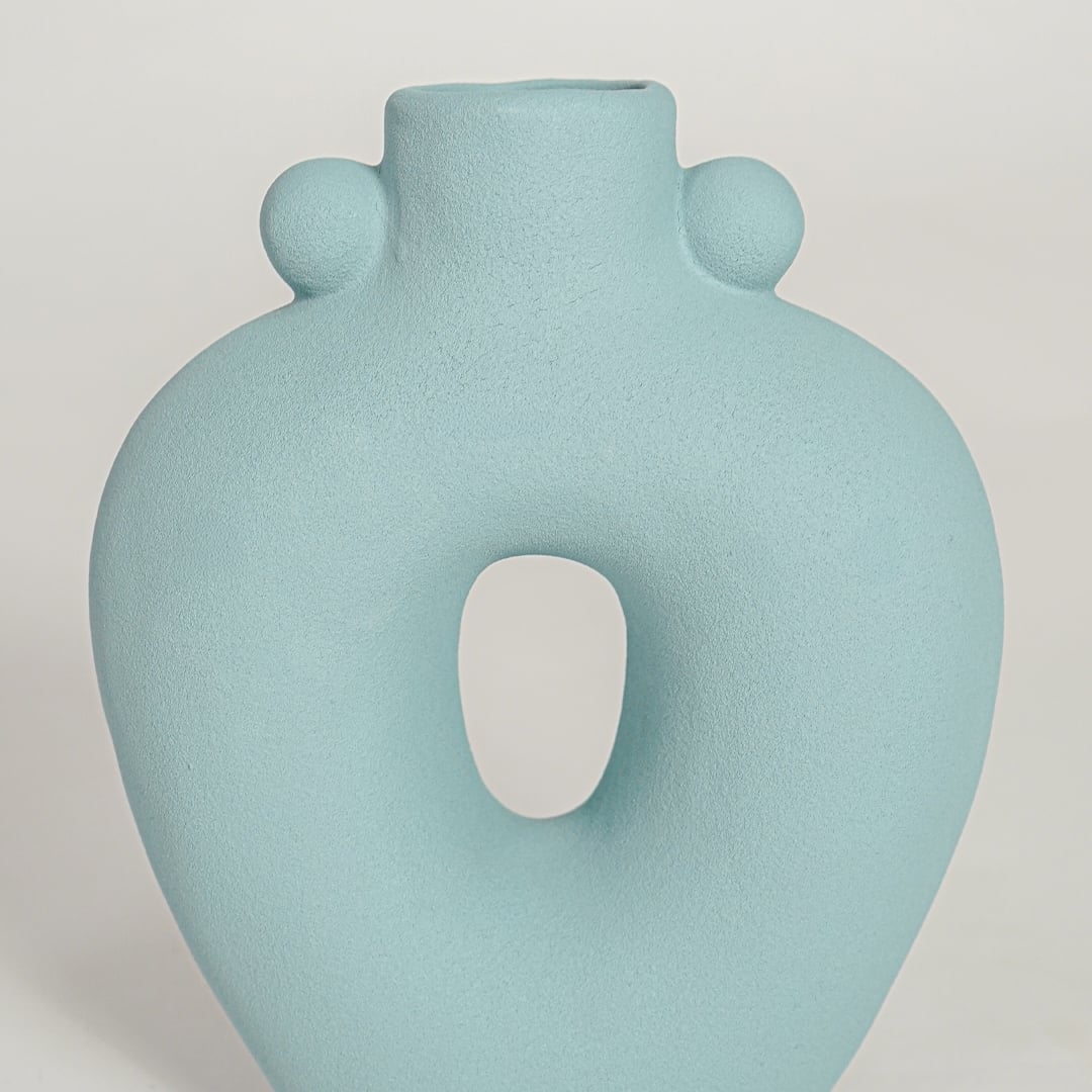 Closeup of matte light blue ceramic vase with curved hollow center ideal for elegant home decor shelf styling.
