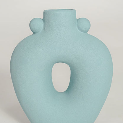 Closeup of matte light blue ceramic vase with curved hollow center ideal for elegant home decor shelf styling.