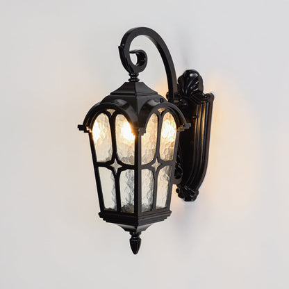 Black exterior wall lantern switched on over white background spreading soft warm illumination through patterned glass.