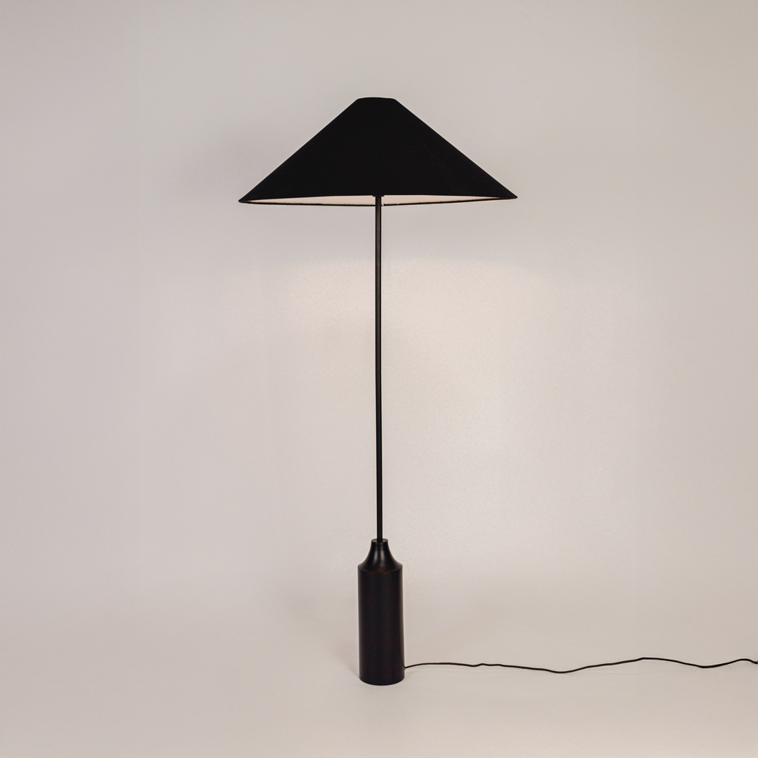 Floor lamp shown on white background with light switched on highlighting fabric shade smooth stacked base and clean modern silhouette.