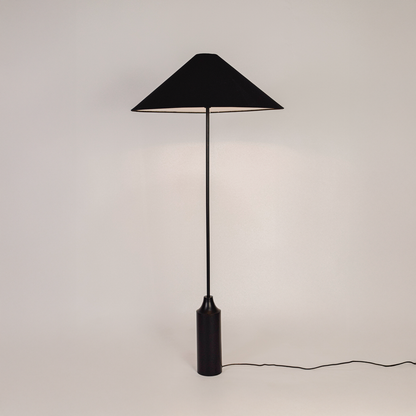 Floor lamp shown on white background with light switched on highlighting fabric shade smooth stacked base and clean modern silhouette.