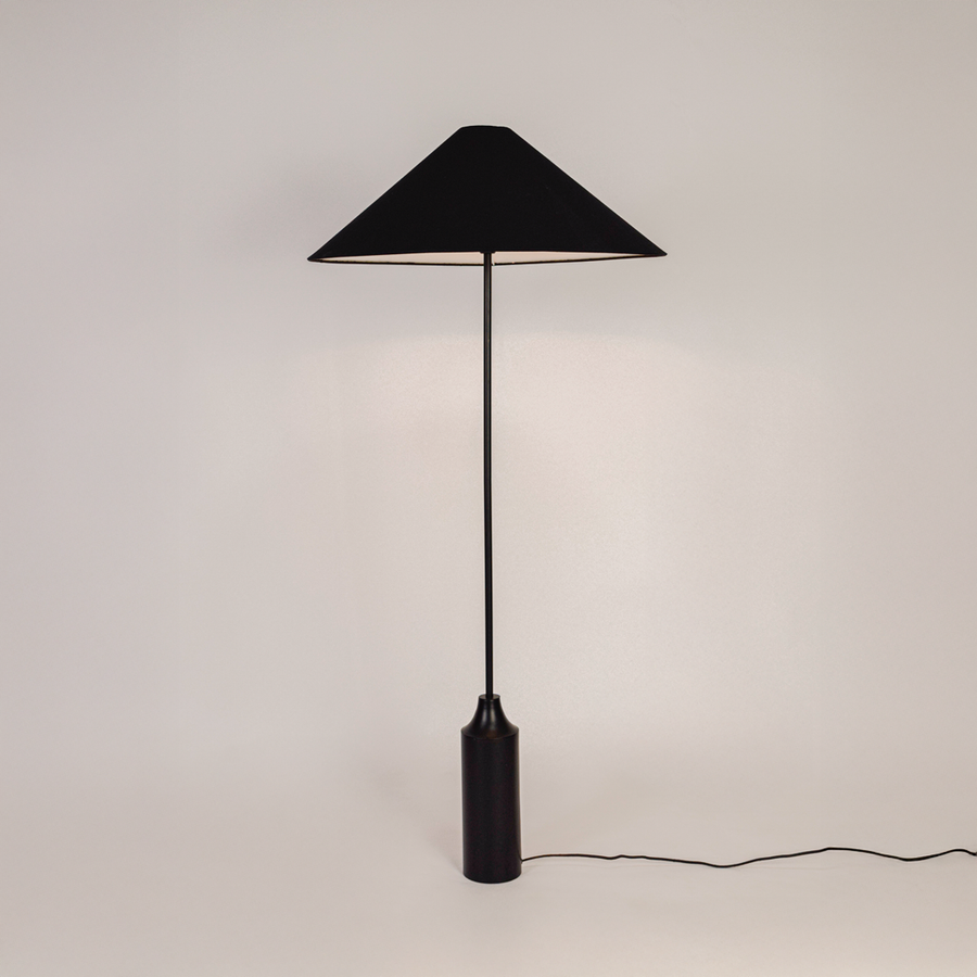 Floor lamp shown on white background with light switched on highlighting fabric shade smooth stacked base and clean modern silhouette.