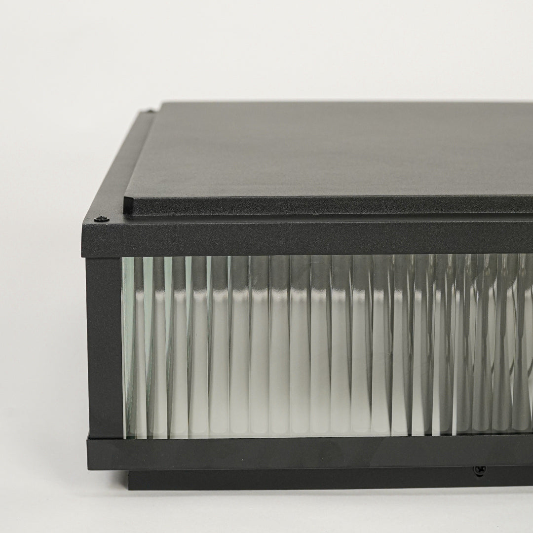 Black outdoor wall light with rectangular metal frame and ribbed glass shade mounted on neutral background ideal for modern exterior lighting.