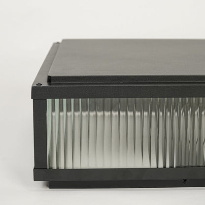 Black outdoor wall light with rectangular metal frame and ribbed glass shade mounted on neutral background ideal for modern exterior lighting.