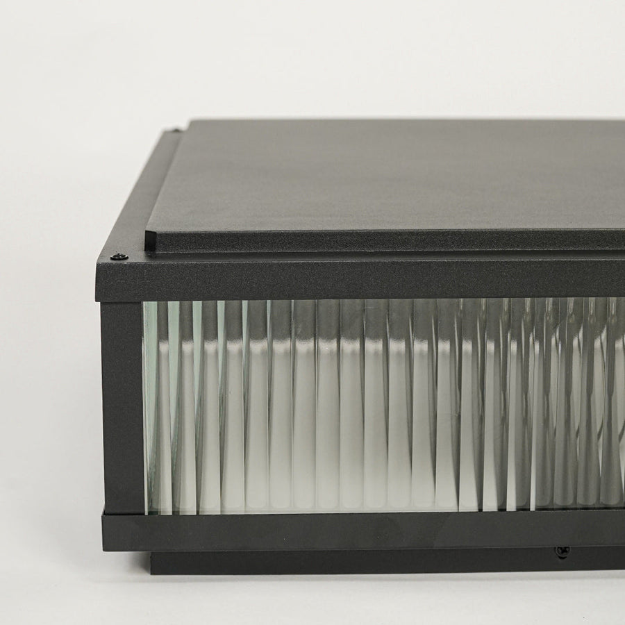 Black outdoor wall light with rectangular metal frame and ribbed glass shade mounted on neutral background ideal for modern exterior lighting.
