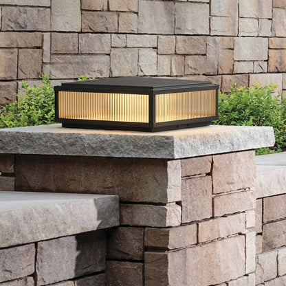 Outdoor pillar light with black metal frame and warm glowing glass installed on stone wall in garden setting ideal for landscape lighting.