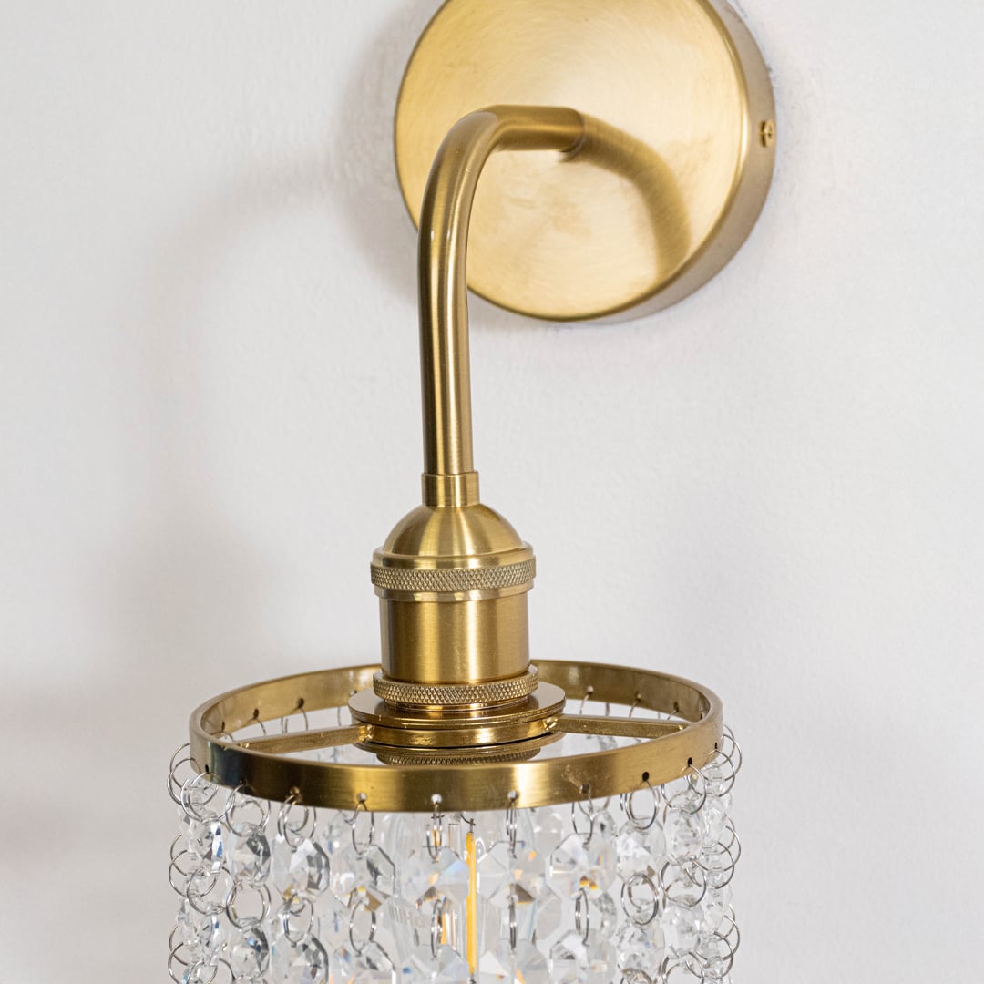 Closeup image of gold metal crystal wall light with transparent hanging crystals for elegant modern interior decor.