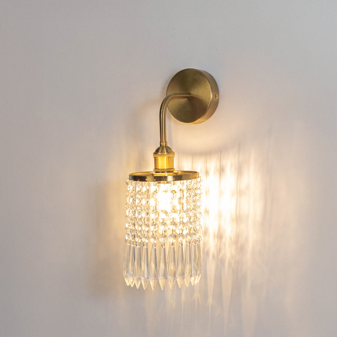 Decorative metal wall light in gold finish with crystal diffuser for warm ambient lighting decor placement in living room white background.