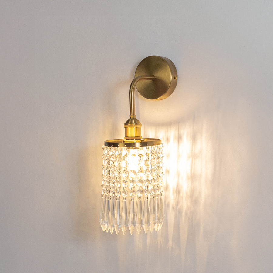 Decorative metal wall light in gold finish with crystal diffuser for warm ambient lighting decor placement in living room white background.