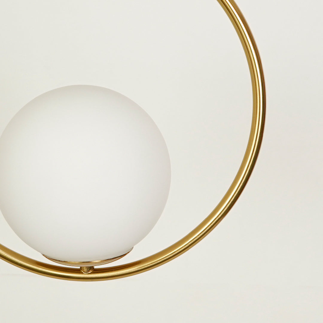 Closeup of gold metal ring pendant light with opal glass globe for elegant contemporary interior lighting display.