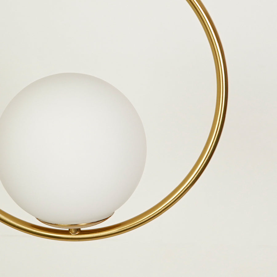 Closeup of gold metal ring pendant light with opal glass globe for elegant contemporary interior lighting display.