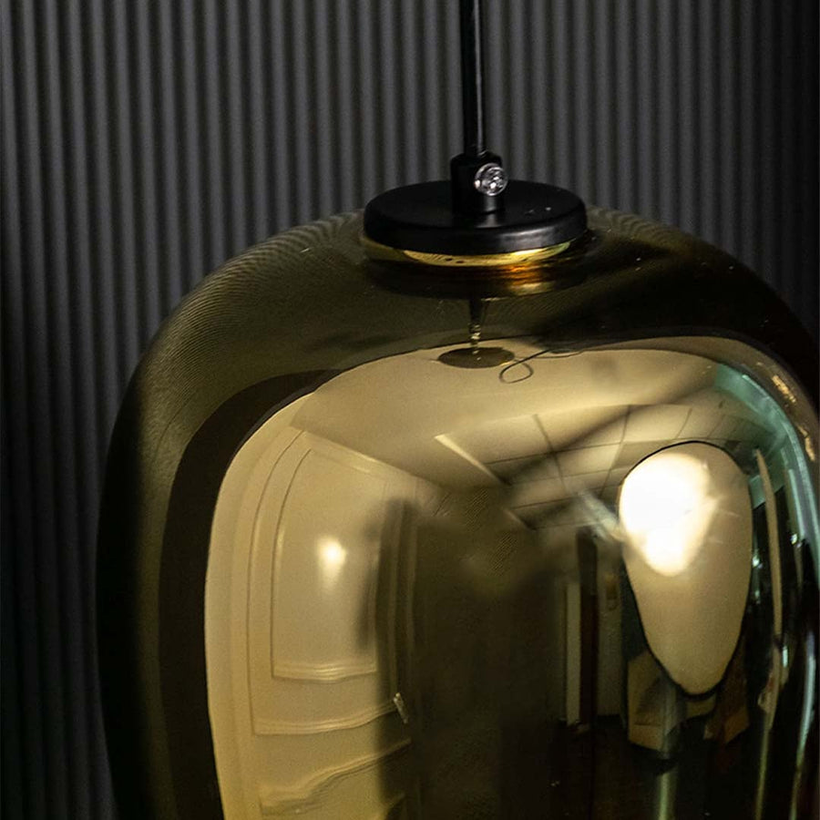 A closeup of the amber tinted glass pendant light highlighting its warm glowing bulb and smooth curved teardrop shaped glass body.