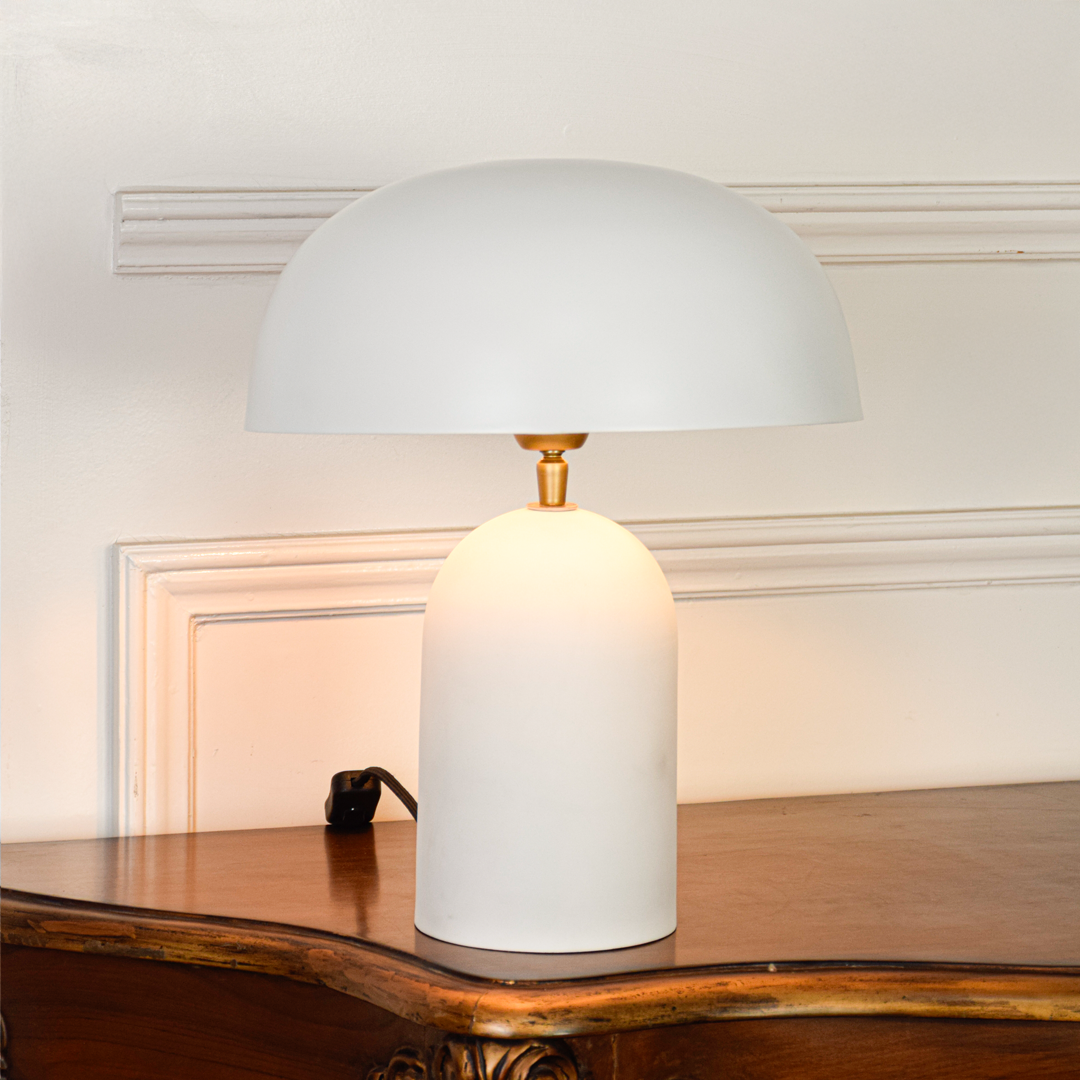 Table lamp displayed on clean white background highlighting rounded white dome shade matte body and brass detail showing modern minimalist design appeal.