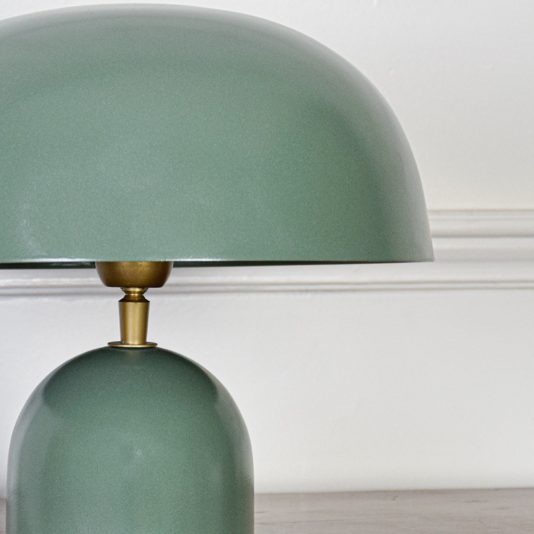 Closeup view of green metal dome shade with soft reflection showing smooth finish brass connector detail and premium tabletop lighting design.