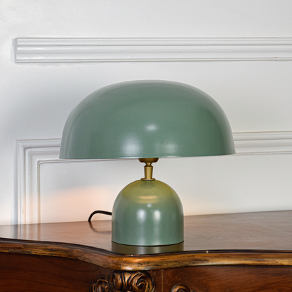 Green dome table lamp switched on against clean white background showing smooth metal shade warm glow compact base and modern home styling.