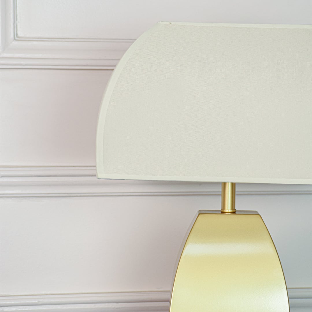Closeup of gold metal table lamp showing smooth satin surface curved silhouette and frosted glass shade texture.