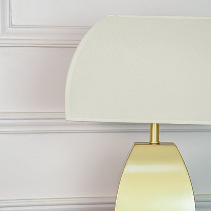 Closeup of gold metal table lamp showing smooth satin surface curved silhouette and frosted glass shade texture.