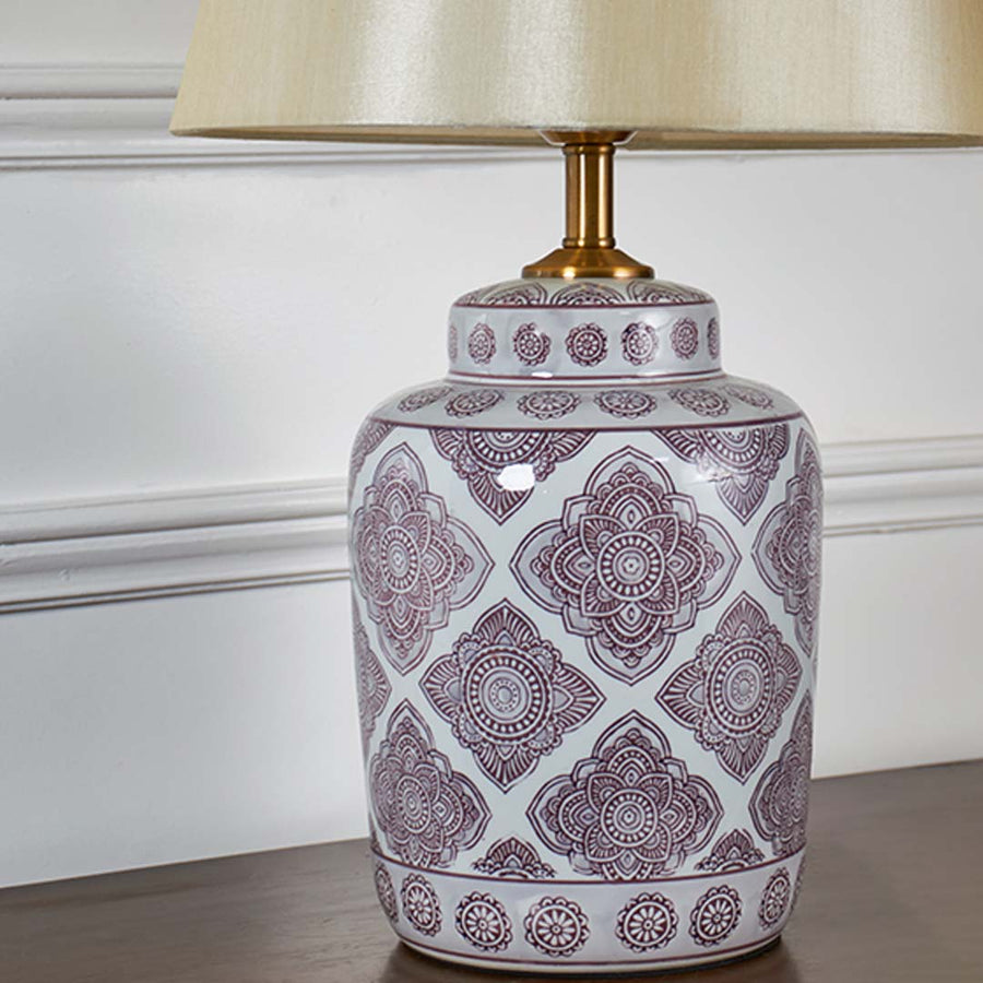 Closeup view of white ceramic lamp base with intricate printed pattern and gold detailing for home lighting decor.