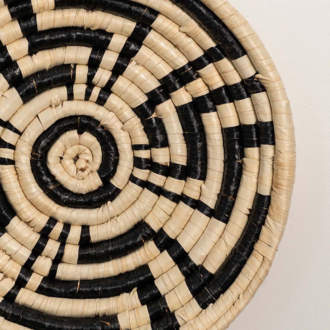 A closeup view of the natural and black rattan wall decor plate showing its detailed woven texture and geometric handcrafted pattern for warm earthy home styling.