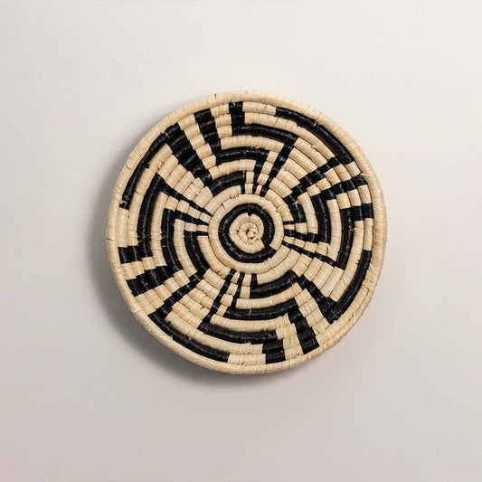 Round handcrafted black and cream woven seagrass wall basket with abstract spiral zigzag pattern on white background image.