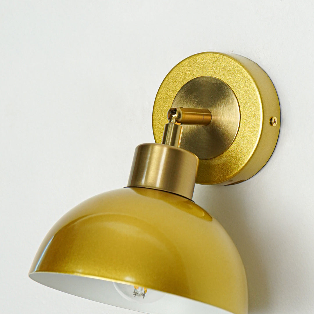 Closeup of gold metal wall light with dome shade showcasing smooth finish and premium detailing for modern interior decor styling.