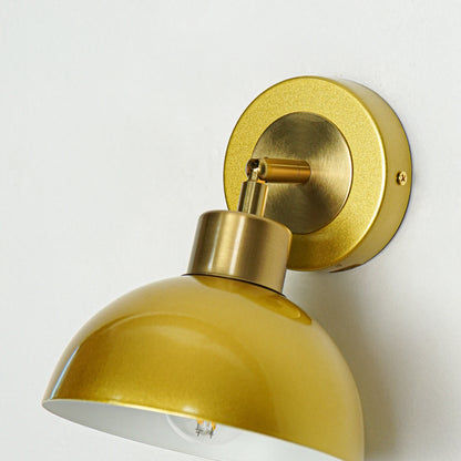 Closeup of gold metal wall light with dome shade showcasing smooth finish and premium detailing for modern interior decor styling.