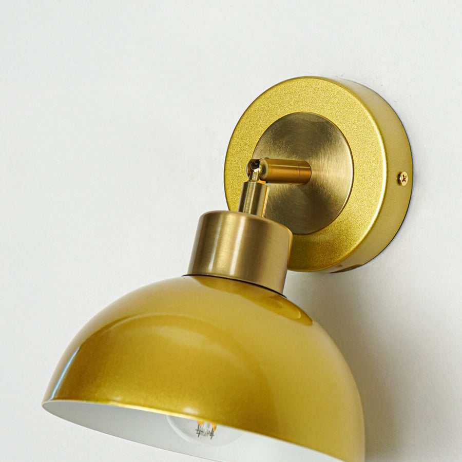 Closeup of gold metal wall light with dome shade showcasing smooth finish and premium detailing for modern interior decor styling.