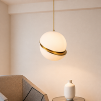 A modern spherical pendant light with a frosted white globe shade and a polished gold metallic band, hanging in a minimalist room setting.