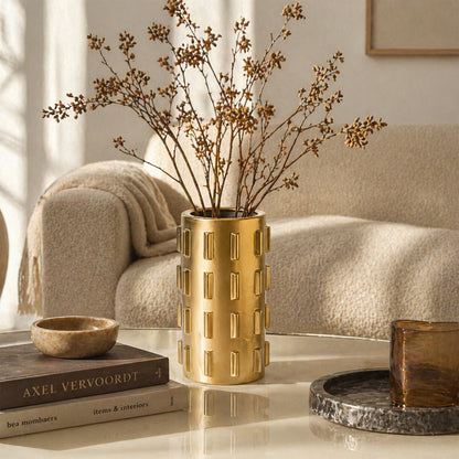 Gold metal flower vase with dried branches placed on table for elegant modern home decor styling.