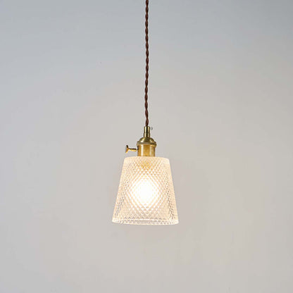 Textured clear glass pendant light with brass top and brown cord glowing warmly on white background for home interiors.